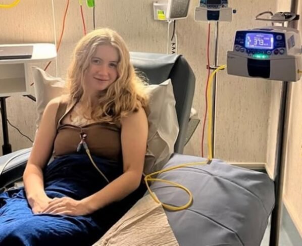 Imagem mostra Dominique McShain, uma mulher jovem, branca e loira, sentada em uma maca de hospital - Metrópoles