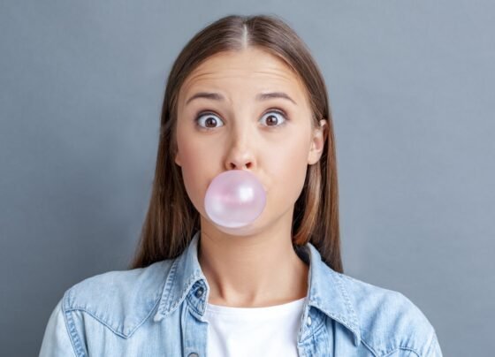 Foto colorida de mulher fazendo bola com chiclete - Metrópoles