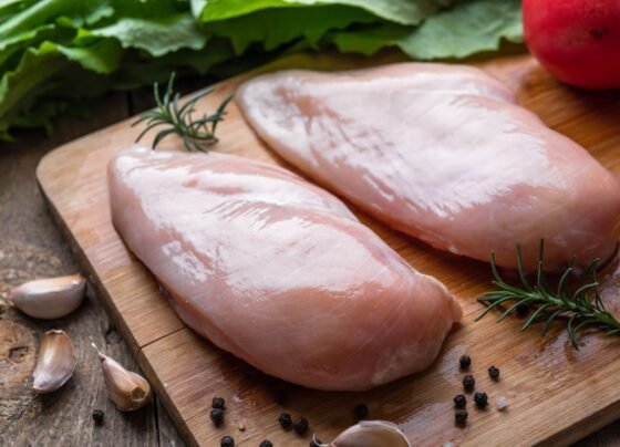Foto colorida de dois peitos de frango cru em uma tábua de madeira - Metrópoles
