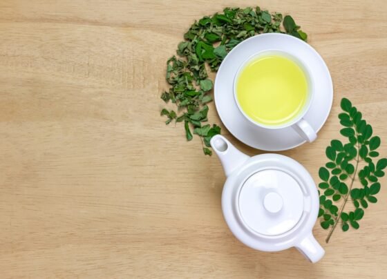 Chá Moringa em xícara branca e folha verde fresca com bule em fundo de madeira, vista superior. Moringa oleifera erva tropical conceito de estilo de vida saudável.