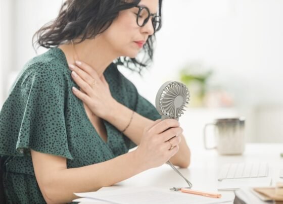Imagem ilustrativa de melhor na menopausa se refrescando com ventilador na mão - Metrópoles
