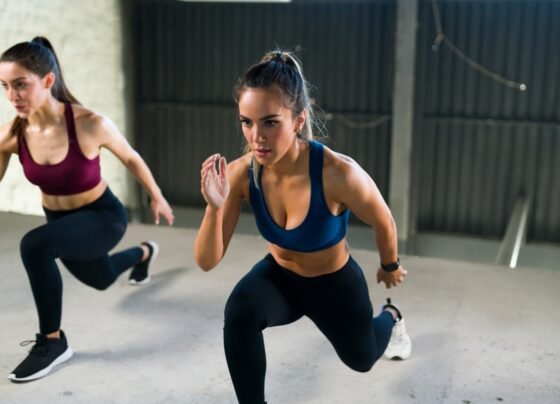 Jovem atlética com um estilo de vida saudável fazendo estocadas nas pernas durante uma aula de HIIT. Mulheres malhando juntas na academia de ginástica