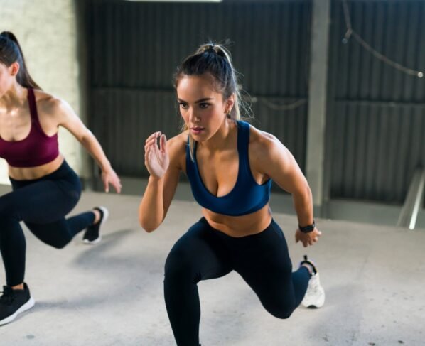 Jovem atlética com um estilo de vida saudável fazendo estocadas nas pernas durante uma aula de HIIT. Mulheres malhando juntas na academia de ginástica