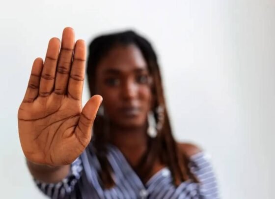 Imagem colorida de uma mulher negra com a palma da mão aberta em sinal de pare - Metrópoles