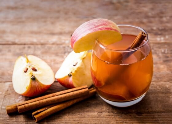 Imagem mostra copo de vidro cheio de chá de maçã, com pedaços da fruta e alguns paus de canela - Metrópoles