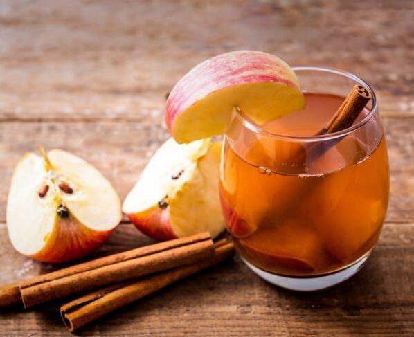 Imagem mostra copo de vidro cheio de chá de maçã, com pedaços da fruta e alguns paus de canela - Metrópoles