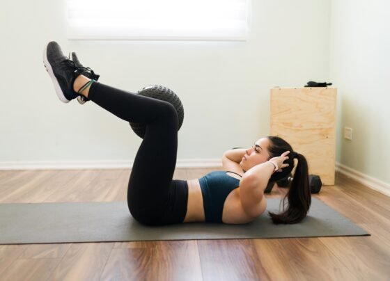 Vista lateral de uma jovem determinada segurando uma bola de slam com as pernas e fazendo abdominais para ter abdominais planos