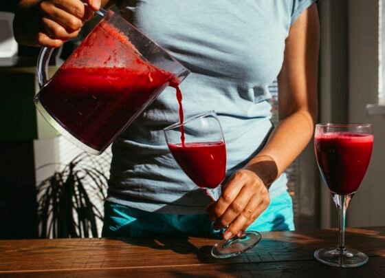 Foto colorida de mulher colocando suco de beterraba em uma taça. Outra taça já tem a bebida - Metrópoles