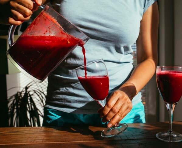 Foto colorida de mulher colocando suco de beterraba em uma taça. Outra taça já tem a bebida - Metrópoles