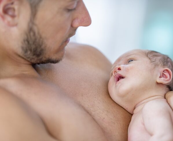 Um pai embala seu bebê recém-nascido contra seu peito nu. Metrópoles