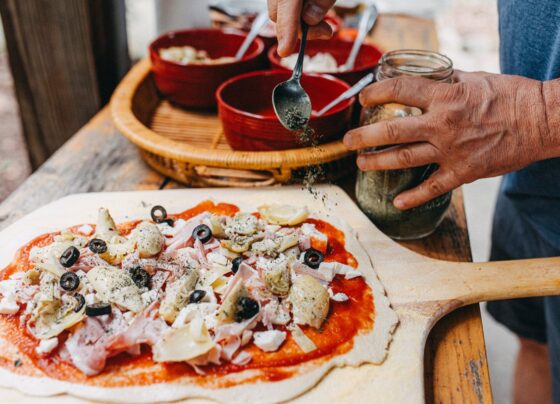 homens temperando uma pizza com orégano - Metrópoles