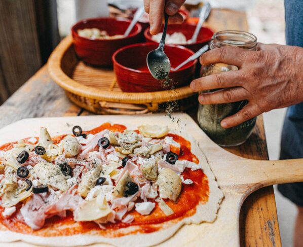 homens temperando uma pizza com orégano - Metrópoles