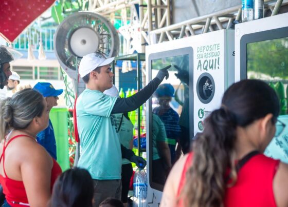 Foto colorida de pessoas depositando garrafas em totens
