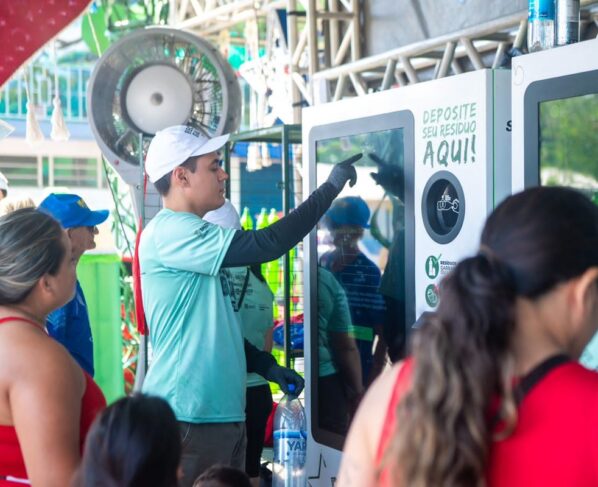 Foto colorida de pessoas depositando garrafas em totens
