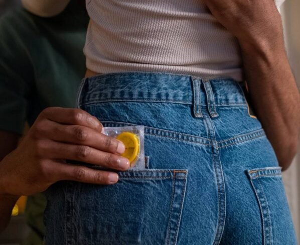 Foto colorida em close de um casal abraçado com o homem colocando uma camisinha no bolso de trás da calça da mulher - Metrópoles