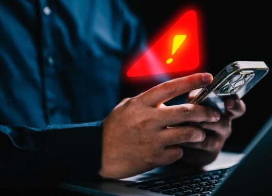 Imagem colorida de pessoa segurando celular com alerta de atenção em cima