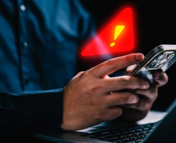 Imagem colorida de pessoa segurando celular com alerta de atenção em cima