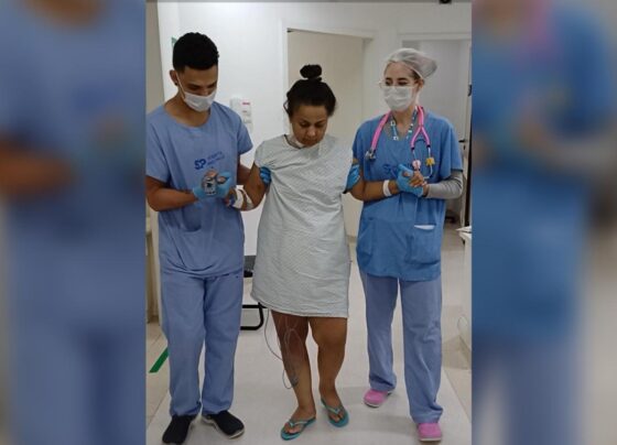 Imagem mostra mulher em hospital sendo amparada por dois profissionais de saúde - Metrópoles