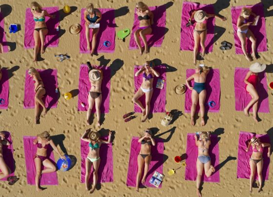 Foto colorida de pessoas pegando sol na praia - Bronzeamento natural: entenda riscos e cuidados da exposição ao sol