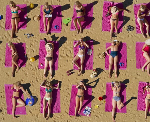 Foto colorida de pessoas pegando sol na praia - Bronzeamento natural: entenda riscos e cuidados da exposição ao sol