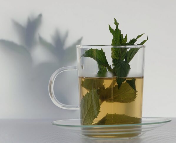 Foto colorida _ Xícara com bebida verde e folhas de hortelã dentro