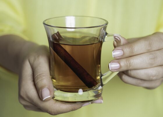 Foto colorida de uma mulher com blusa amarela segurando uma xícara de chá de canela - Metrópoles.