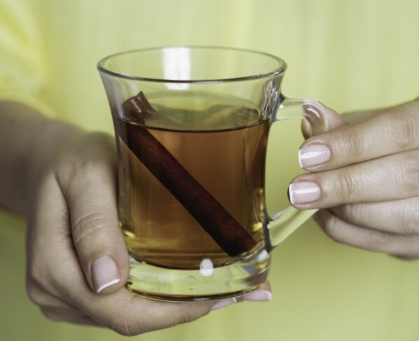 Foto colorida de uma mulher com blusa amarela segurando uma xícara de chá de canela - Metrópoles.