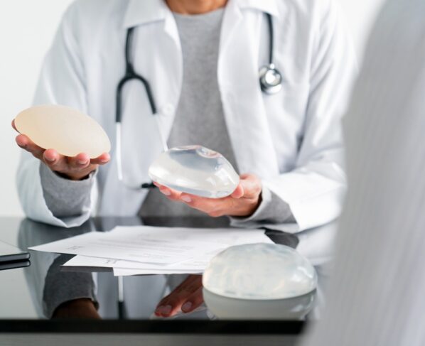 Close-up de um cirurgião plástico comparando dois tipos de implantes mamários em seu consultório - conceitos de saúde e medicina. Metrópoles