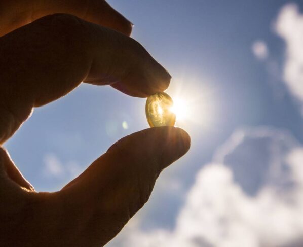 Foto colorida - Mão segurando um comprimido na frente do sol - vitamina d