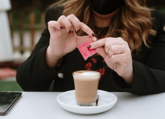 Imagem de mulher colocando adoçante em copo com bebida marrom - Metrópoles