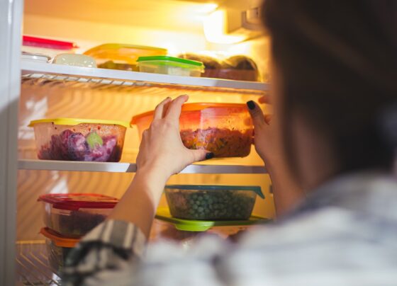 Imagem mostra mulher guardando potes de vidro tampados com comida na geladeira - Metrópoles
