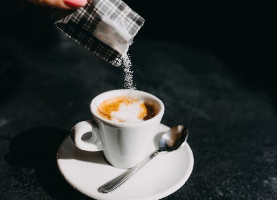 Imagem colorida mostra adoçante ou açúcar sendo despejado em xícara de café - Metrópoles