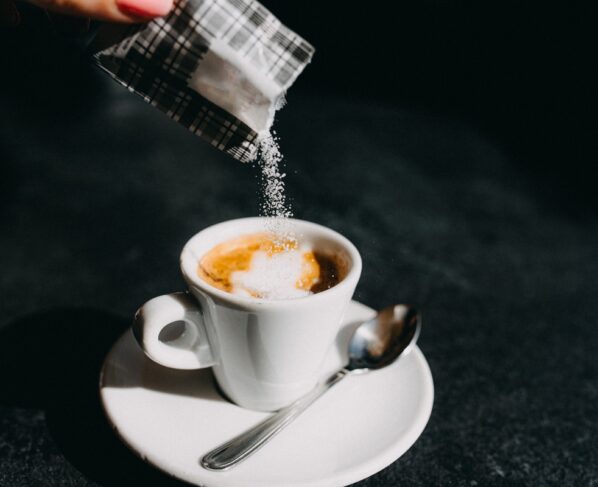 Imagem colorida mostra adoçante ou açúcar sendo despejado em xícara de café - Metrópoles