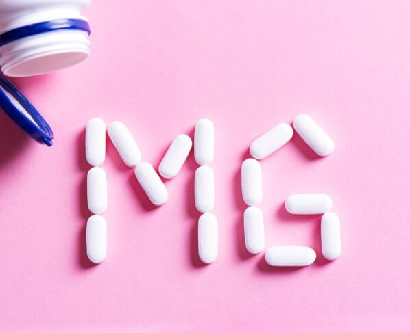 Pote de suplementos aberto em cima da mesa com pílulas formando "MG"