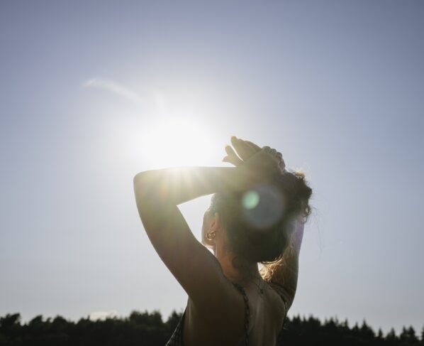 Imagem mostra mulher com os braços para cima recebendo a luz do sol - Metrópoles
