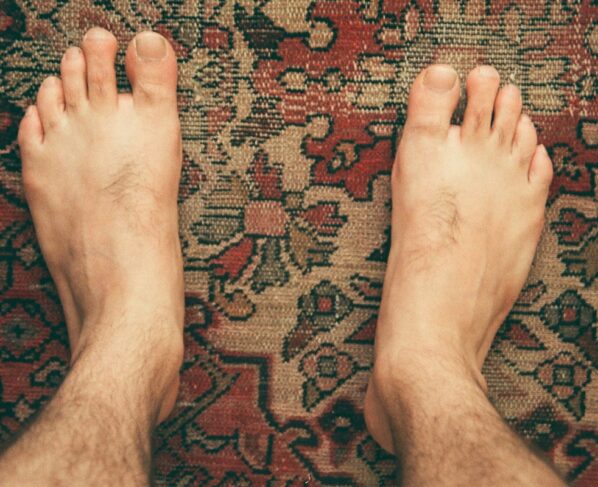 Foto colorida de pés sobre um tapete estampado - Metrópoles.