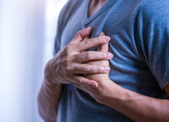Foto colorida de um homem com blusa azul e mãos no peito, com sintomas de infarto - Metrópoles.
