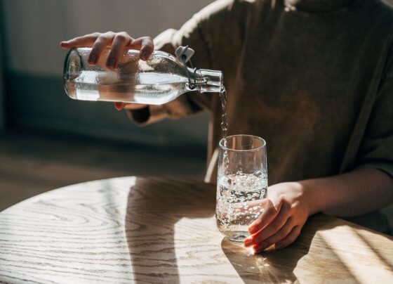 Foto colorida de mulher enchendo copo de água - Ortopedistas explicam se beber água ajuda em casos de hérnia de disco - Metrópoles