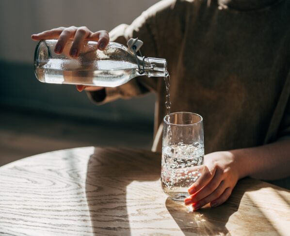 Foto colorida de mulher enchendo copo de água - Ortopedistas explicam se beber água ajuda em casos de hérnia de disco - Metrópoles