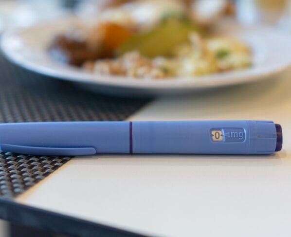 Uma caneta Ozempic em um guardanapo ao lado de um prato de comida não saudável, conceito de tratamento médico, controle do diabetes e escolhas de estilo de vida. Metrópoles