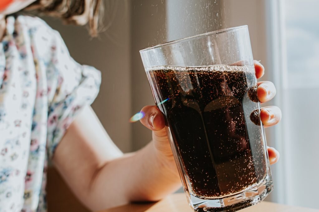 Foto colorida de mulher segurando copo de refrigerante coca - Metrópoles