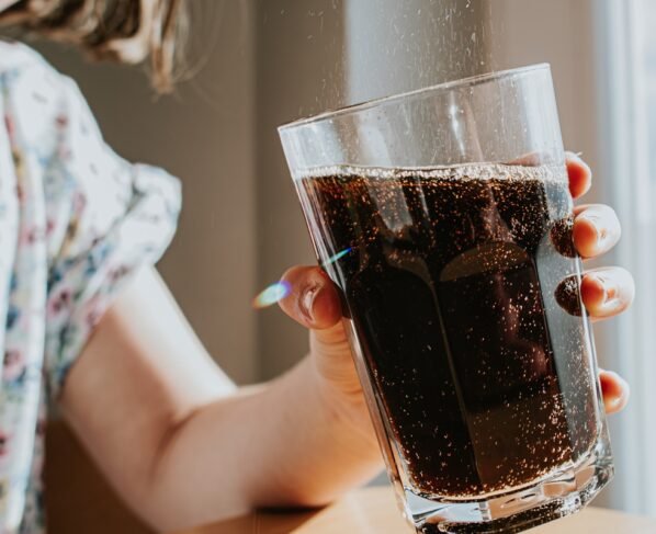 Foto colorida de mulher segurando copo de refrigerante coca - Metrópoles