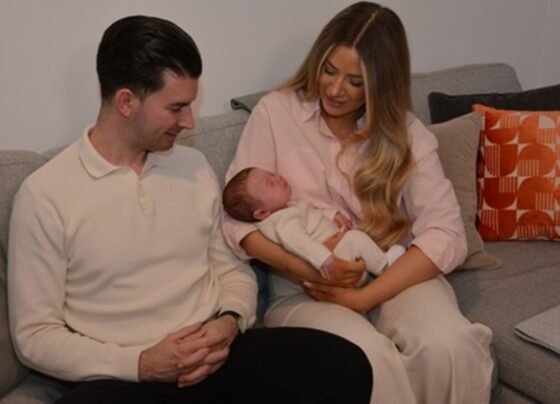Foto colorida de familia com bebê recém-nascido no colo, resultad de transplante de útero em sucedido - Metrópoles.