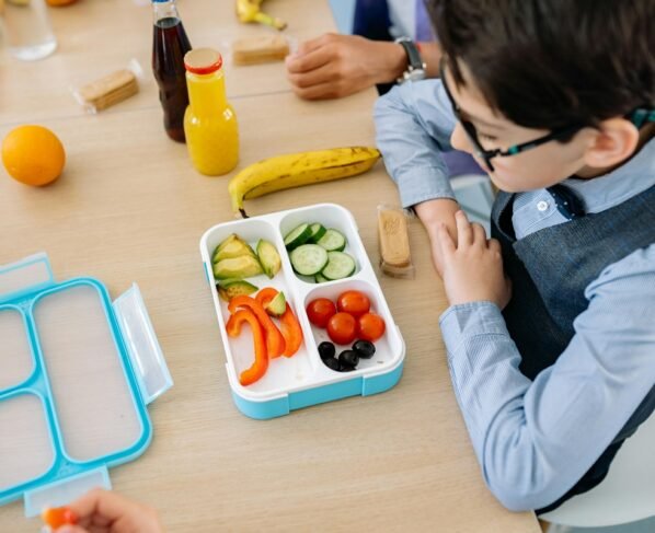 Foto colorida de criança comendo comida saudável da lancheira - Nutricionista infantil lista melhores alimentos para ter na lancheira - Metrópoles