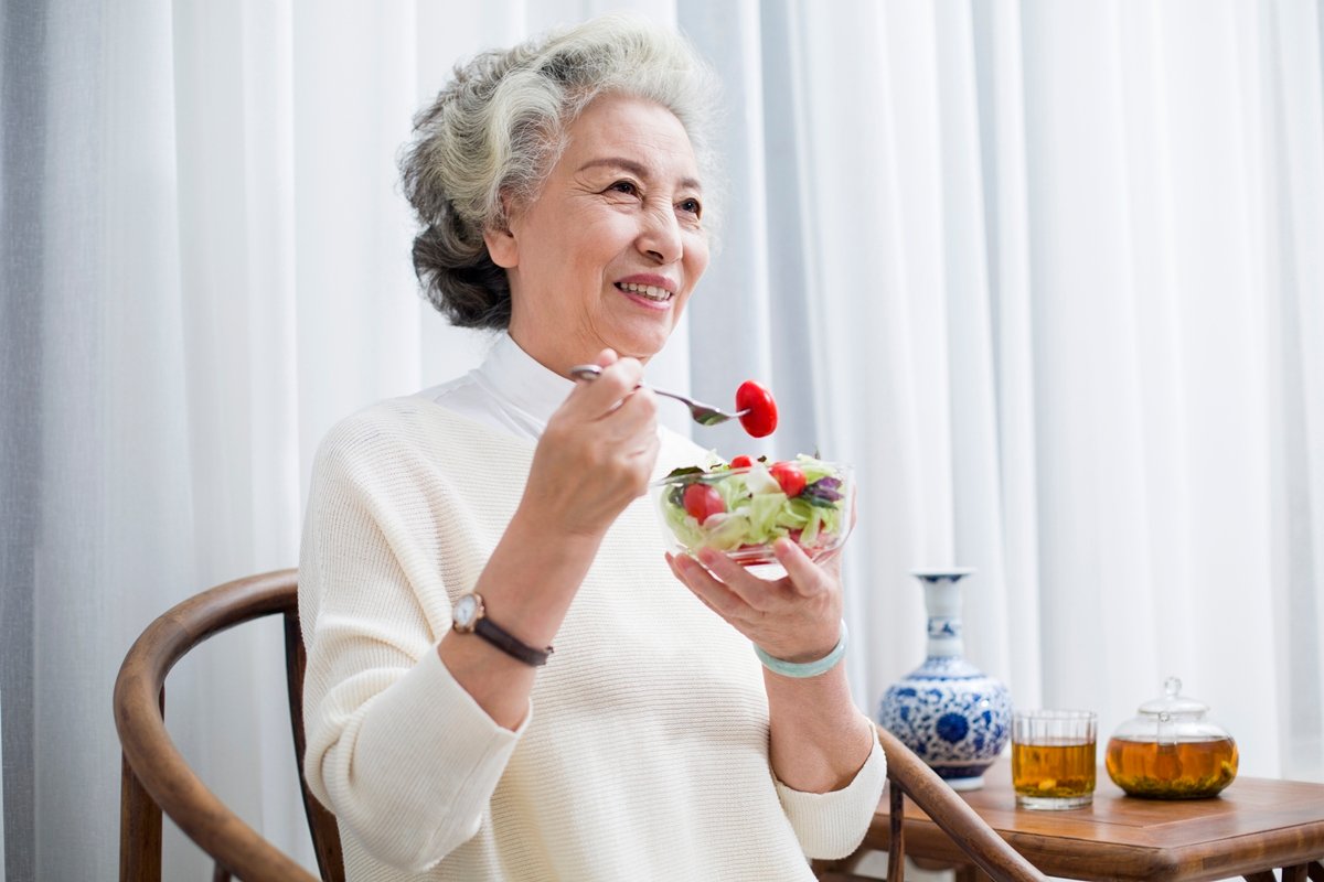 Foto colorida de mulher segurando tigela com frutas. Ela está levando garfo com fruta à boca - Metrópoles