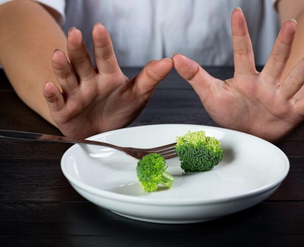 Mãos de mulher empurrando prato com brócolis - Metrópoles