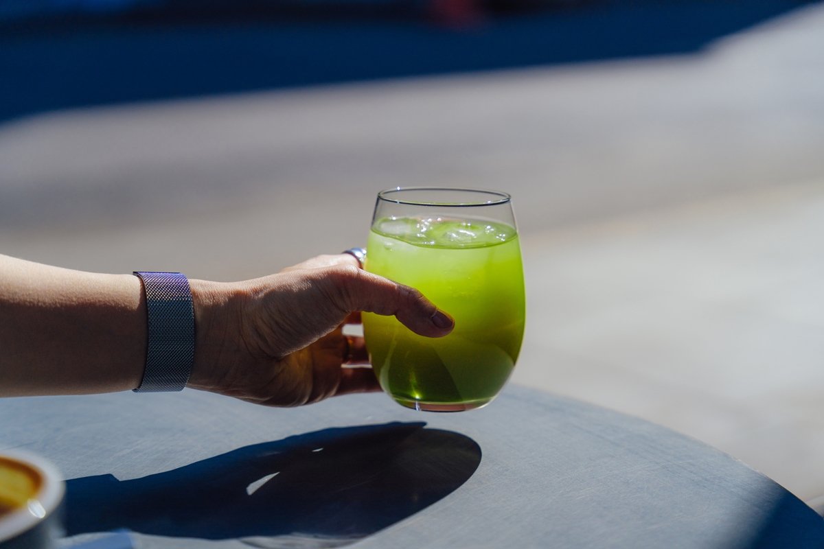 Mão feminina segurando um copo de suco verde, feito com couve, pepino, aipo e suco de limão, sobre uma mesa em um café na calçada. Estilo de vida saudável. Dieta detox com sucos. Bebidas detox. Metrópoles