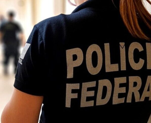 Imagem colorida mostra mulher de costas vestindo colete preto onde está escrito Polícia Federal - Metrópoles