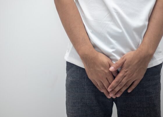 Imagem mostra homem com camiseta branca e calça preta com as mãos sobre as partes íntimas - Metrópoles