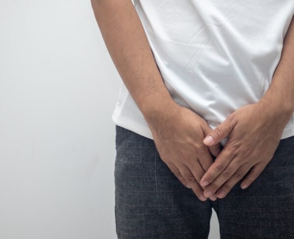 Imagem mostra homem com camiseta branca e calça preta com as mãos sobre as partes íntimas - Metrópoles